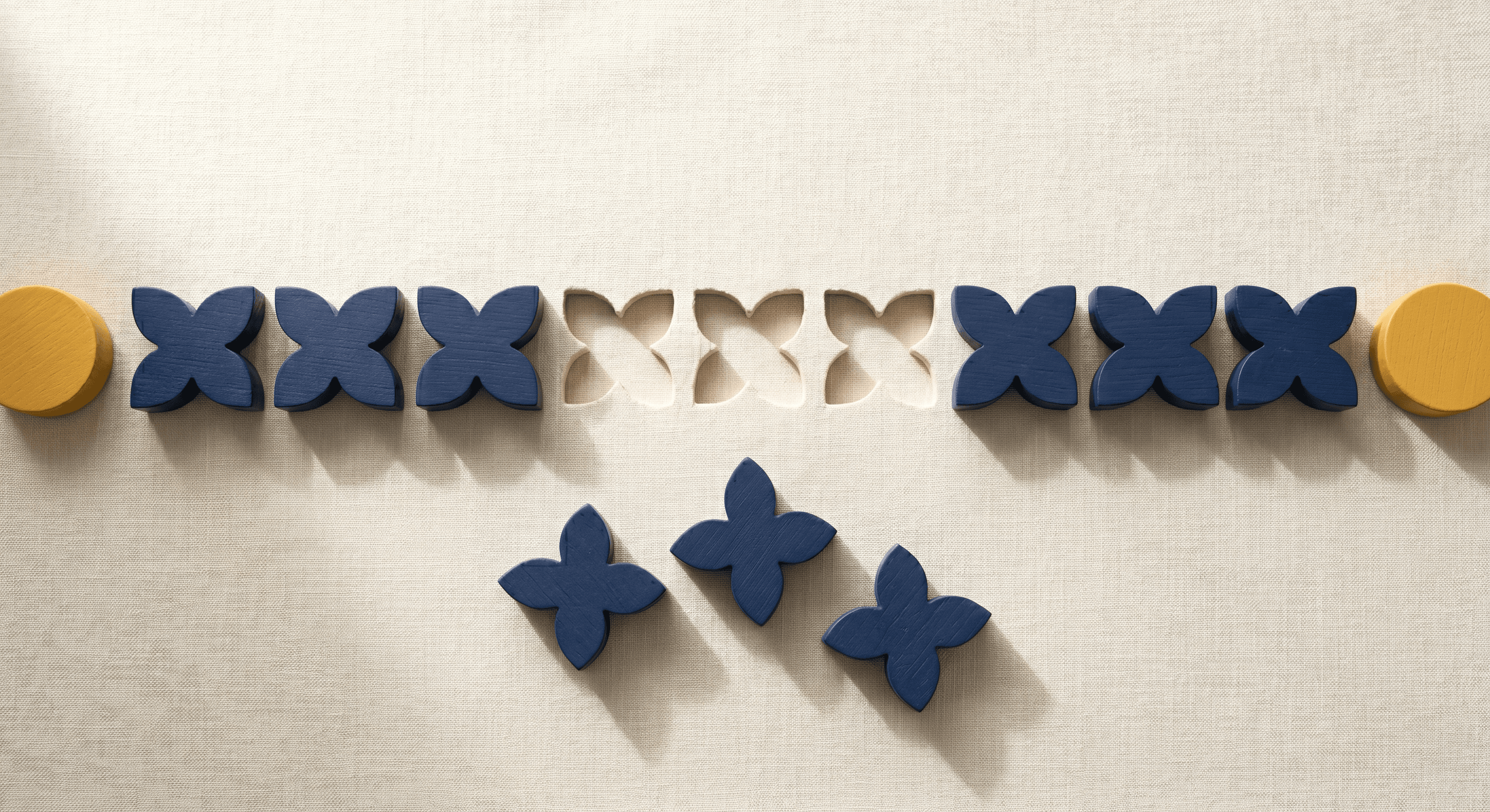 Row of navy wooden four-petal shapes with three removed and clustered below the line on cream linen