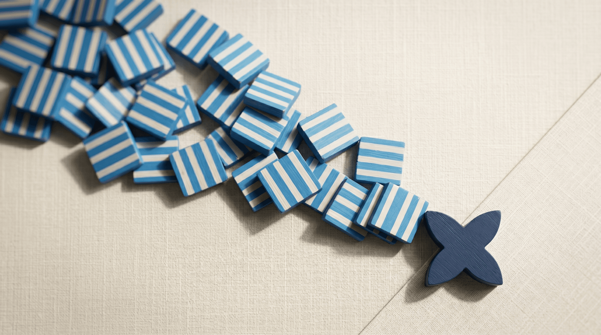 Cascade of blue striped squares spilling diagonally with a navy four-petal shape blocking the flow on cream linen