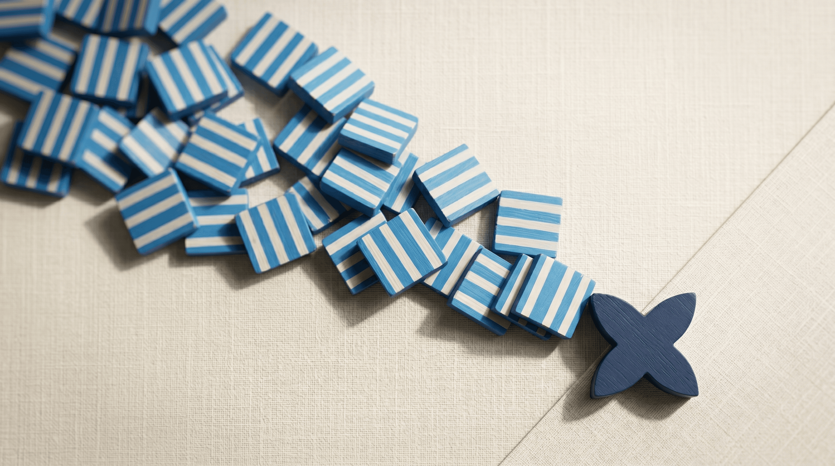 Cascade of blue striped squares spilling diagonally with a navy four-petal shape blocking the flow on cream linen